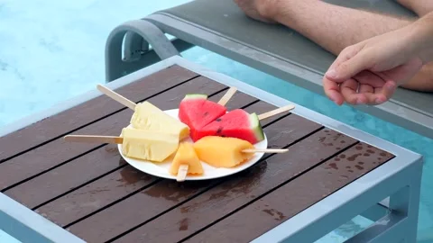 Young man having fun in the pool with fruit plate with watermelon, pineapple and 動画素材 237334564