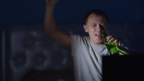 Young man having fun sitting with a bottle of beer at night in front of the TV Stock Footage 137869574