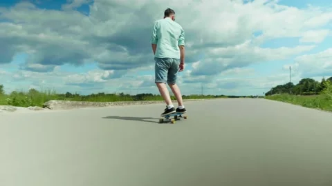 Young man having fun skateboarding alone on a road. View from the back Stock Footage 134064225