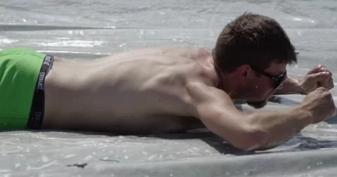 Young man having fun slipping around on a slip and slide in the summer heat Stock Footage 52669928