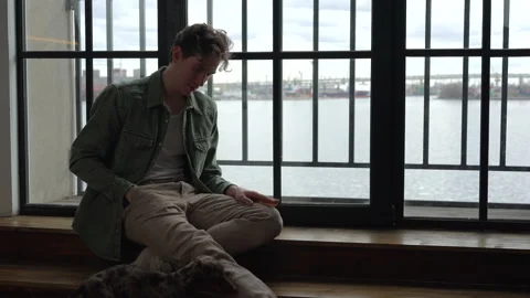 Young man is having good time with dog and sitting by window in home room spbd. Stock Footage 198827329
