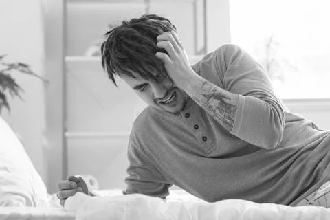 Young man having panic attack on bed at home Stock Photos