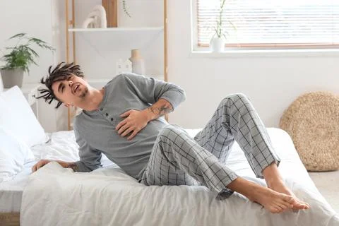 Young man having panic attack on bed at home Stock Photos