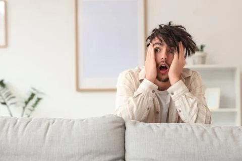 Young man having panic attack behind sofa at home Stock Photos