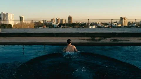 Young man having a refreshing dip in the rooftop pool above the city Foto stock