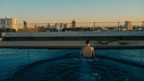 Young man having a refreshing dip in the rooftop pool above the city Stock Photos