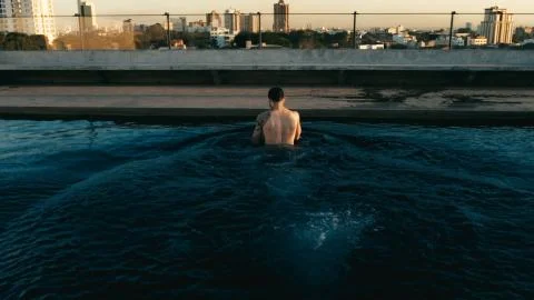 Young man having a refreshing dip in the rooftop pool above the city Stock Photos
