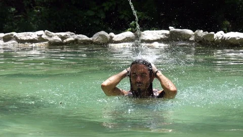 Young man having a shower in splasing water jet in a hot springs Stock Footage 91195346