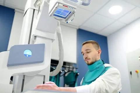 Young man having x-ray shot of broken hand in Xray room in modern clinic. Pat Stock Photos
