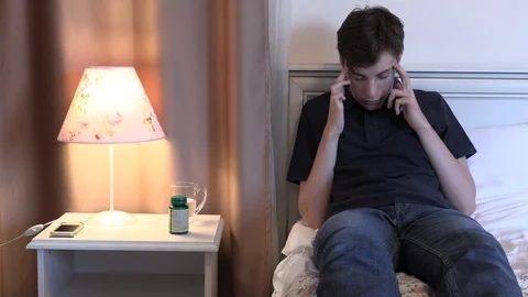 Young man with headache lying on bed massaging and taking pill Stock Footage 106299471