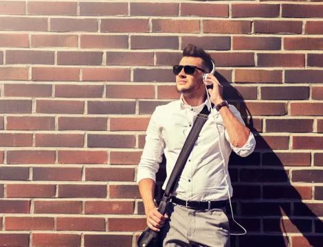 Young man in headphones with bag over brickwall Stock Photos