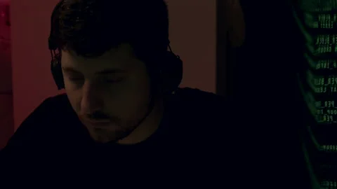 Young man with headphones focused on work in a dimly lit room, illuminated by Stock Footage 313934057