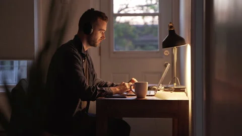 Young Man in Headphones Freelancer Using Laptop in the Evening at home Stock Footage 139725433