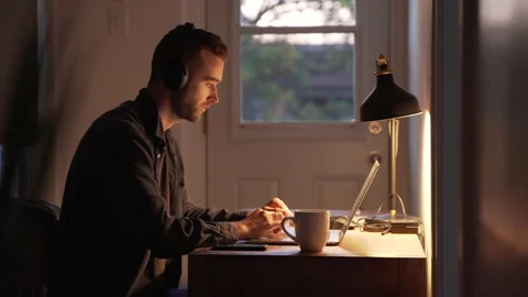 Young Man in Headphones Freelancer Using Laptop in the Evening at home Stock Footage 139726013
