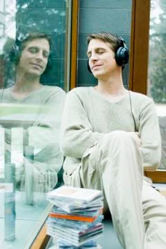 Young man with headphones relaxing on window sill Stock Photos