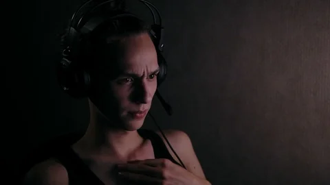 Young man in headphones testing microphone on computer at night Видео 99932028