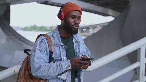 Young man in headphones using smartphone and smiling, standing in urban Stock Footage 163815154