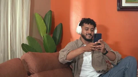 Young man with headphones using smartphone at home Stock Footage 338401003