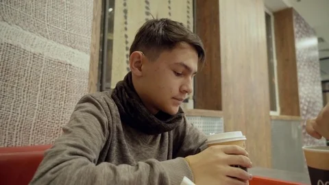 A young man with hearing loss drinks coffee in a cafe from a paper cup. Stock Footage 82516975