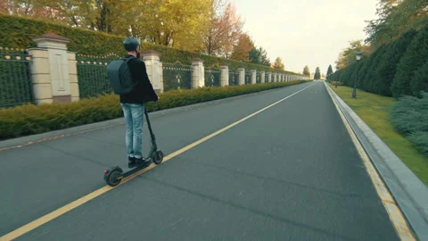 Young man in helmet with backpack riding on fine deserted road on e-scooter Stock Footage 256342500