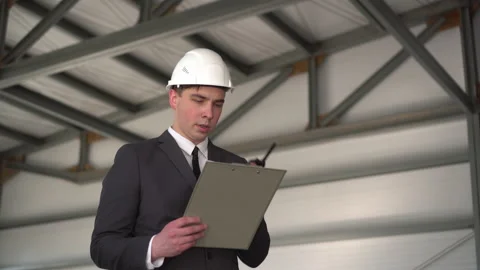 A young man in a helmet with documents speaks on a walkie-talkie at a Video stock 134268605