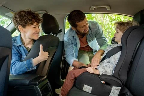 Young man helping his adorable little son with fastening seatbelt in the car Stock Photos