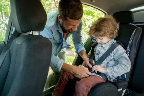 Young man helping his cute little son to put seatbelt while going to countryside Stock Photos