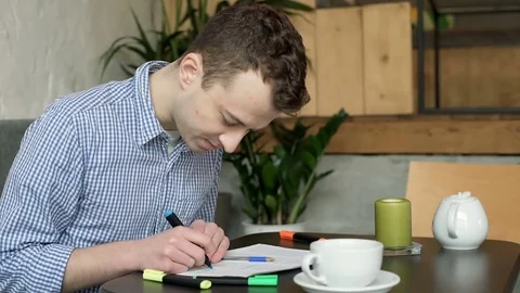 Young man highlights something on his notes and smiles to the camera, steadycam  Stock Footage 72771364