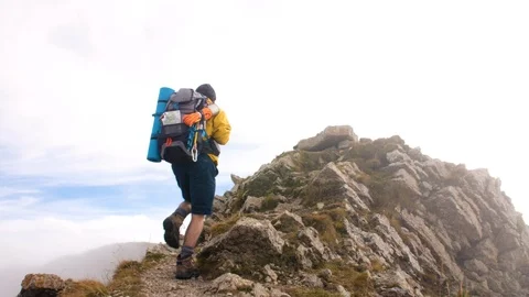 Young man hiker on mountain with cloudy sky and fog. Yellow jacket, backpack and 스톡 동영상 122102848