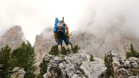 Young man hiker standing on stone mountain raising up arms with cloudy sky and Stock Footage 122000566