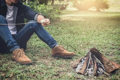 Young Man hiking cooking a marshmallow candies on the campfire in forest, hik Stock Photos
