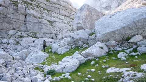 Young man hiking to mountain top walking on rocks and green field scenic view Stock Footage 161909320