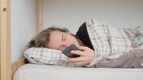 Young man hitting the snooze button on his phone alarm in the morning Stock Footage 310739206