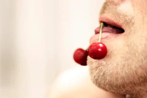 Young man hold a cherry with his seductive tongue Stock Photos