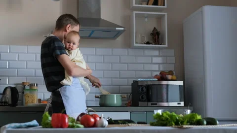 Young man holding baby while cooking in kitchen Stock Footage 227370663