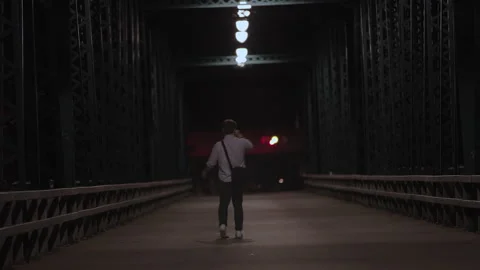 Young man holding a bottle walks alone across an empty, illuminated city bridge Stock Footage 344294629