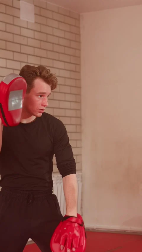 Young man holding boxing pads receiving punches in indoor training room with Stock Footage 343092275