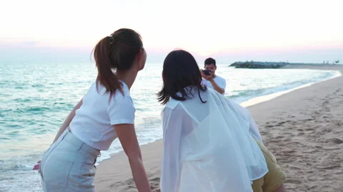 Young man holding camera taking photo of teenage girls posing on beach Видео 171870492