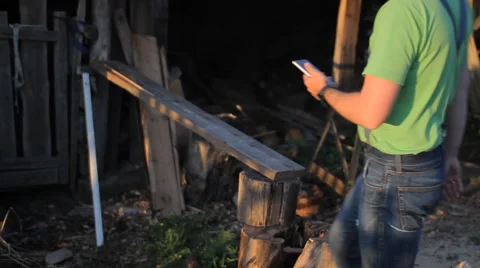 Young man holding a cellphone at sunset. A man sits at the sawmill Stock Footage 64776471