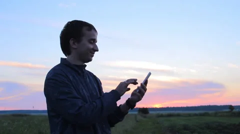 Young man holding a cellphone at sunset. He write sms Stock Footage 64777079