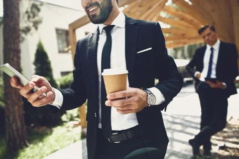 Young man holding cup of coffee while standing with smartphone Stock Photos