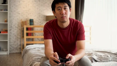 Young man holding game controller while playing video console game. Asian guy Stock Footage 129299141