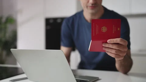 Young man holding German passport while applying for a visa on laptop Stock Footage 337907344