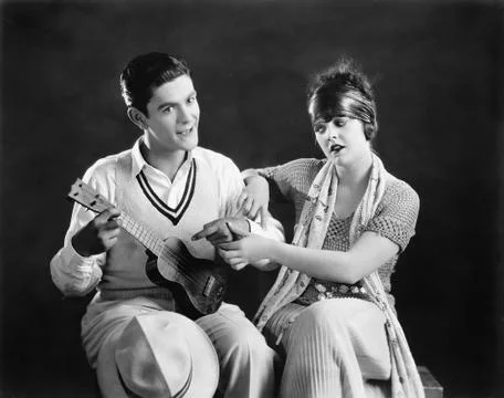 Young man holding a guitar with a young woman teaching him how to play Stock Photos