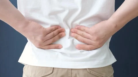 Young man holding his hands on his lower back on blue background close-up Stock Footage 278015616