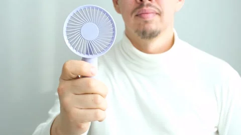 Young man holding mini fan on a gray background close-up, front view. Stock Footage 301162050