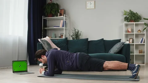 Young man holding plank pose on floor in living room, using video fitness lesson Stock Footage 157369771