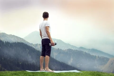Young man holding plastic bottle on rocky summit. Pure nature workout concept Stock Photos