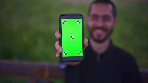 Young Man Holding Smartphone with empty green screen, outdoors Видео 89984821