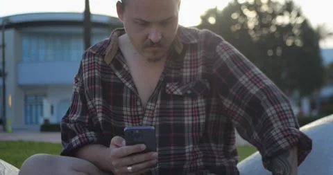 Young Man Holding Smartphone While Sitting Outdoors... Stockbeeldmateriaal 333525083